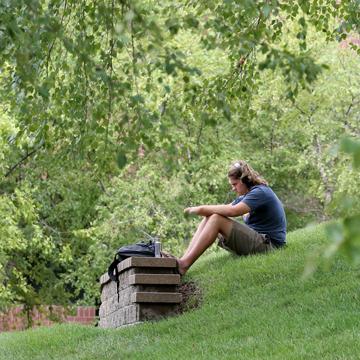 一个学生坐在校园的小山上，戴着耳机听音乐.